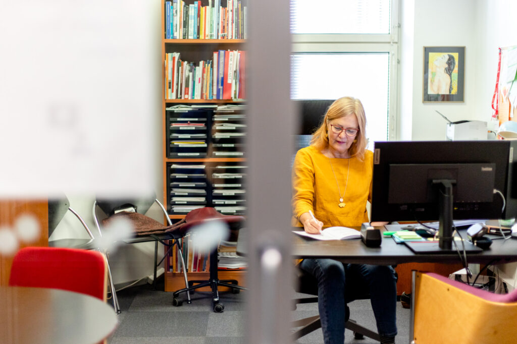 Tarja Muukkonen työkentelee työpöytänsä ääressä syventyen paperiin.