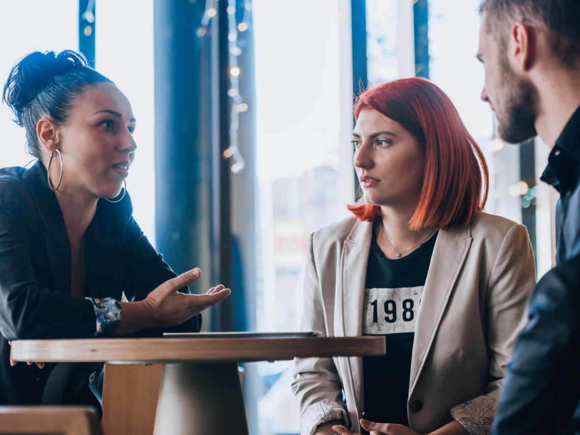 Kolme henkilöä keskustelee keskittyneesti pöydän ympärillä.