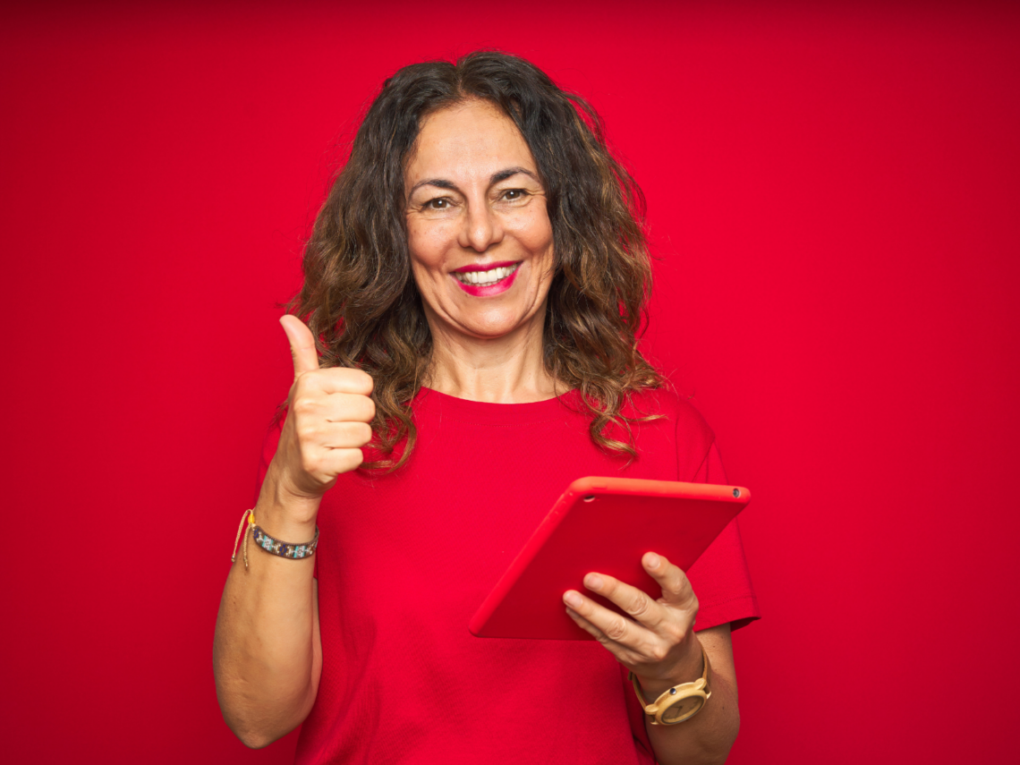 Henkilö pitää toisessa kädessään tablettitietokonetta ja näyttää toisella kädellä peukaloa.