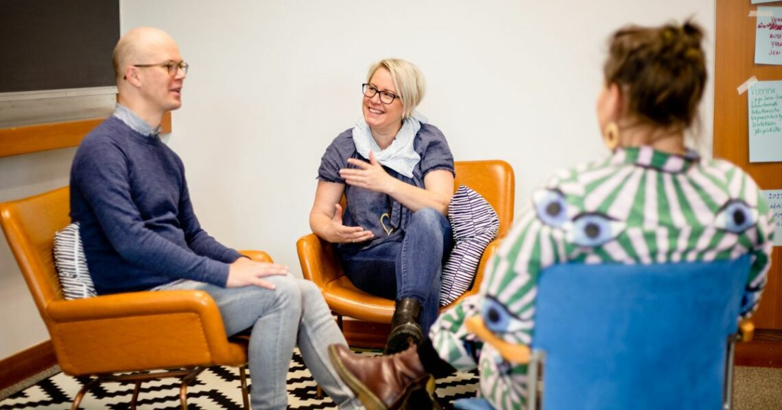 Kolme henkilöä keskustelee tuoleilla istuen.