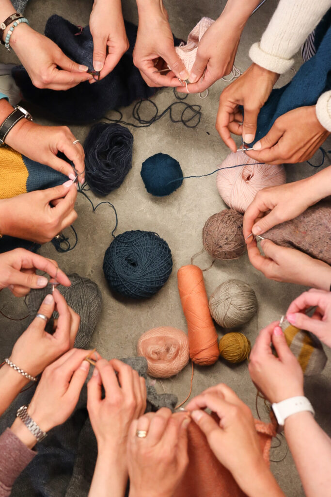 Yhdeksän käsiparia neuloo piirissä.