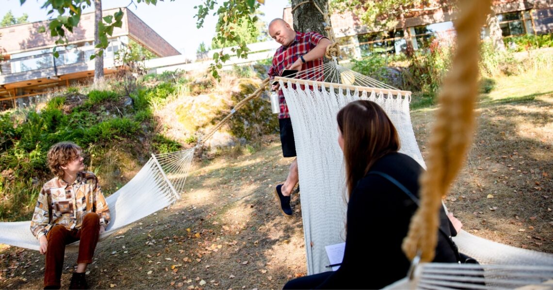 Kaksi henkilöä istuu omissa riippumatoissaan ja kolmas nojailee puuhun.