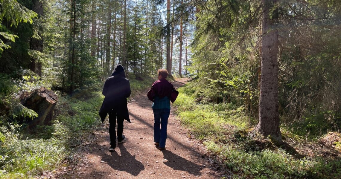 Kaksi henkilöä kävelee kesäisellä metsäpolulla.