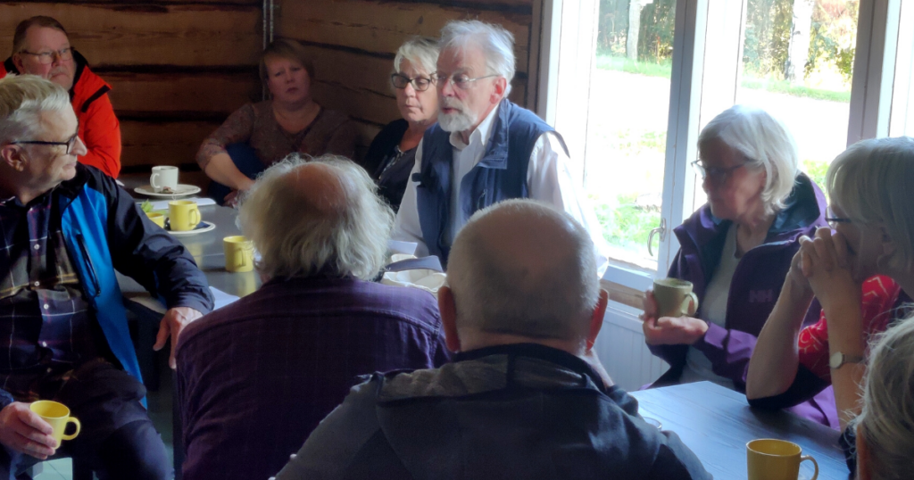 Yhdeksän henkilöä istuu pirtissä keskustelemassa.