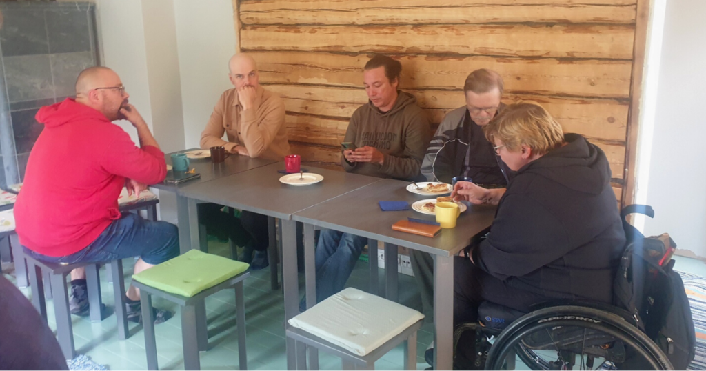 Viisi henkilöä istuu pöydän ääressä mökissä. 