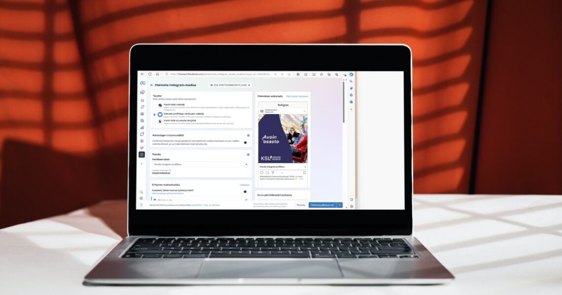 Kannettava tietokone, jonka ruudulla on Instagramin mainostyökalu. Taustalla on punainen verho, johon heijastuu sälekaihtimet.